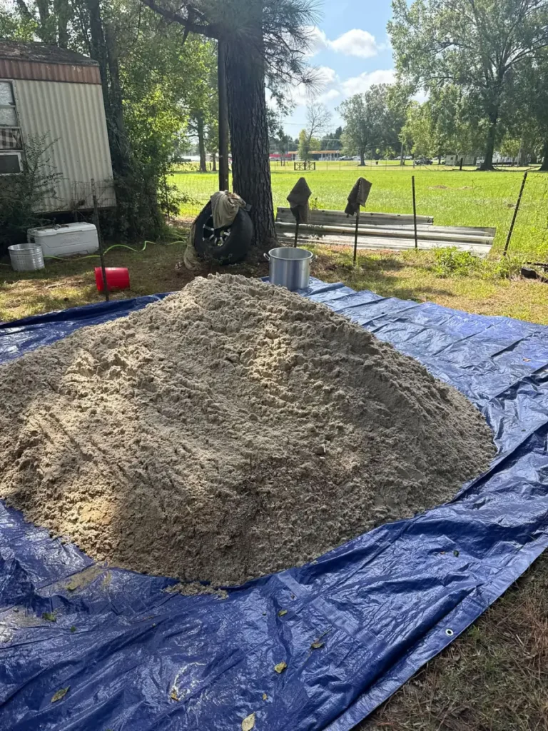 A load of sand dumped onto a blue tarp in a Livingston Parish yard, delivered by dump trailer.