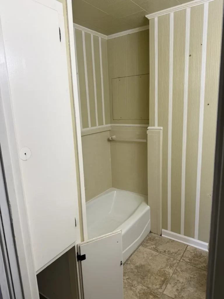 The tub alcove and linen cabinet of the same bathroom before demolition, with paneled walls and tile floor.